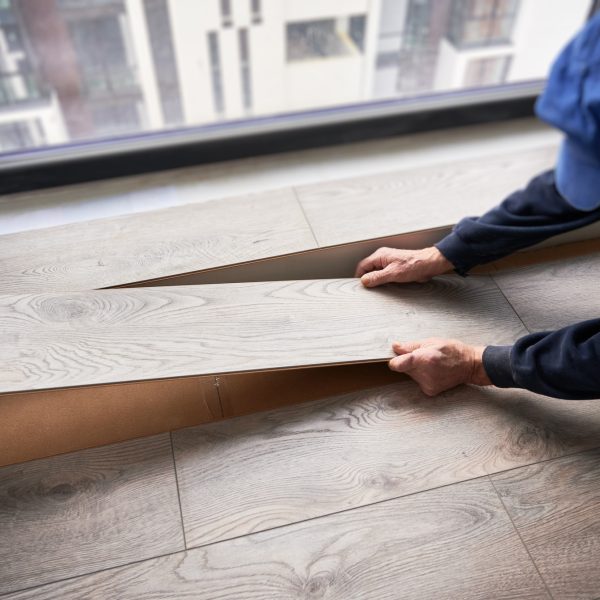 Man laying laminate flooring in apartment under renovation.